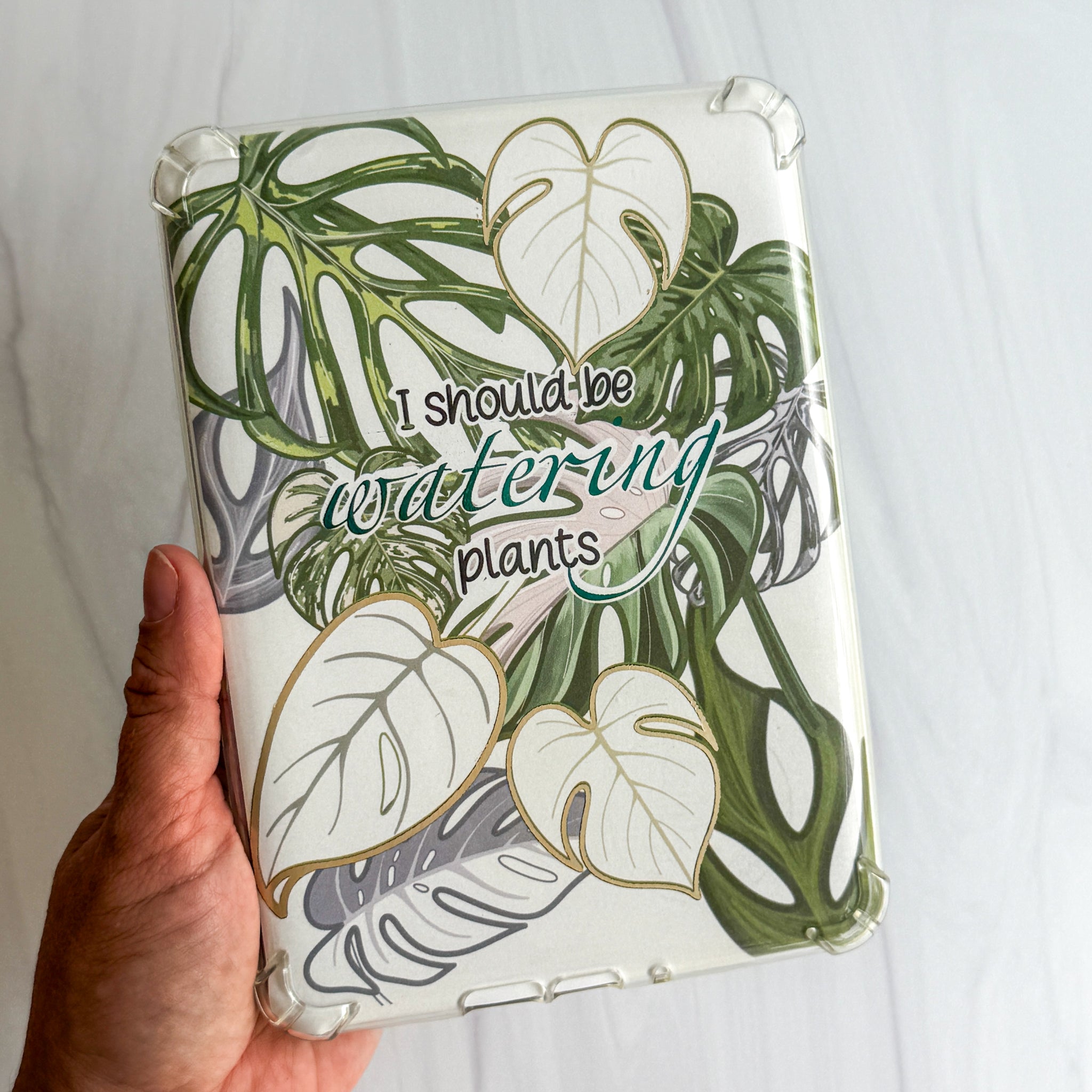 1. I should be watering plants foiled Kindle insert with monstera and alocasia leaves, Kittlins
2. Kittlins plant lover Kindle insert shown under a clear case with a Kindle device nearby (device and case not
included)
3. Close-up of champagne and blue foiled monstera leaf detail on Kindle insert cardstock